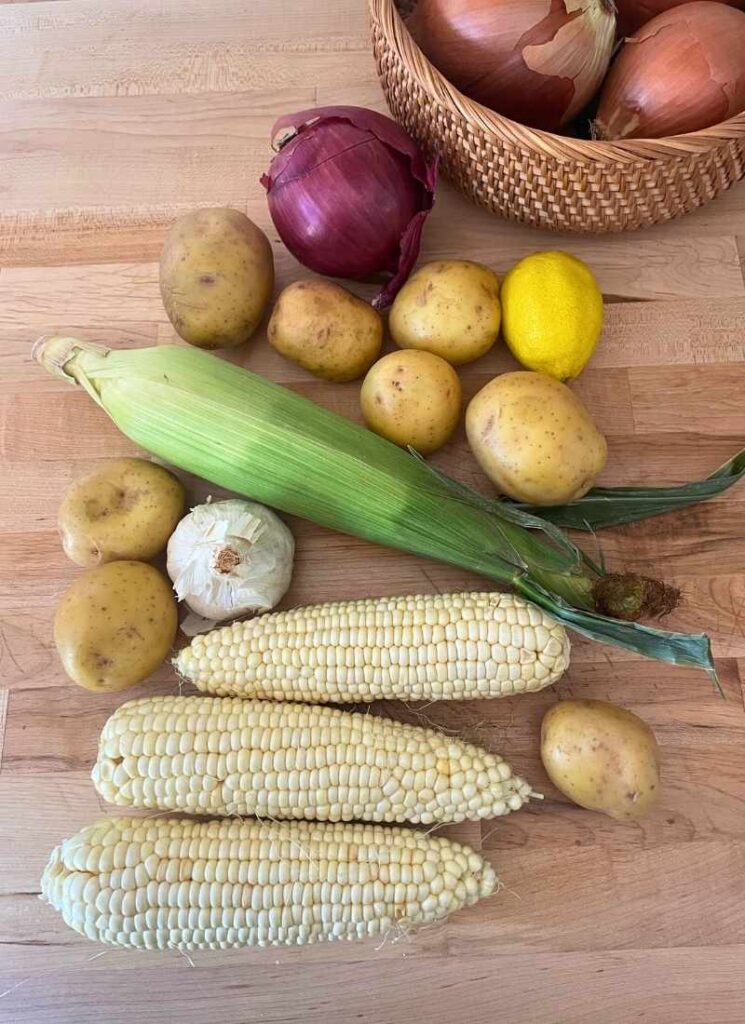 Veggie ingredients for sheet pan corn and shrimp dinner. Fresh corn on the cob, yellow potatoes, garlic, red onion, and lemon of course!