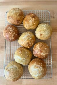 Top-down photo of our whole grain sourdough hamburger buns recipes on the cooling rack topped with sesame seeds